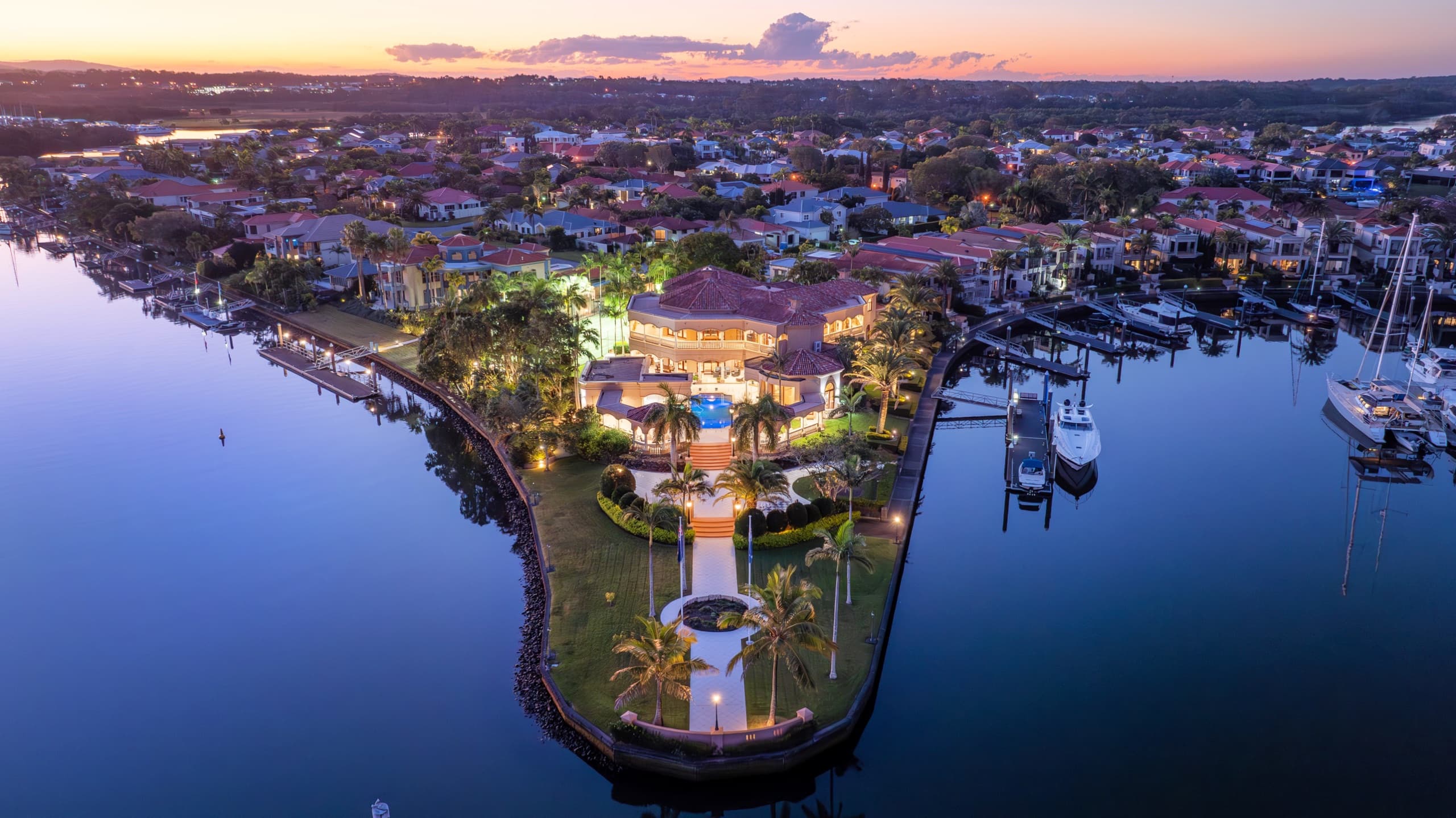 Bellagio Gold Coast — the riverfront estate at dusk, lights reflecting on the water
